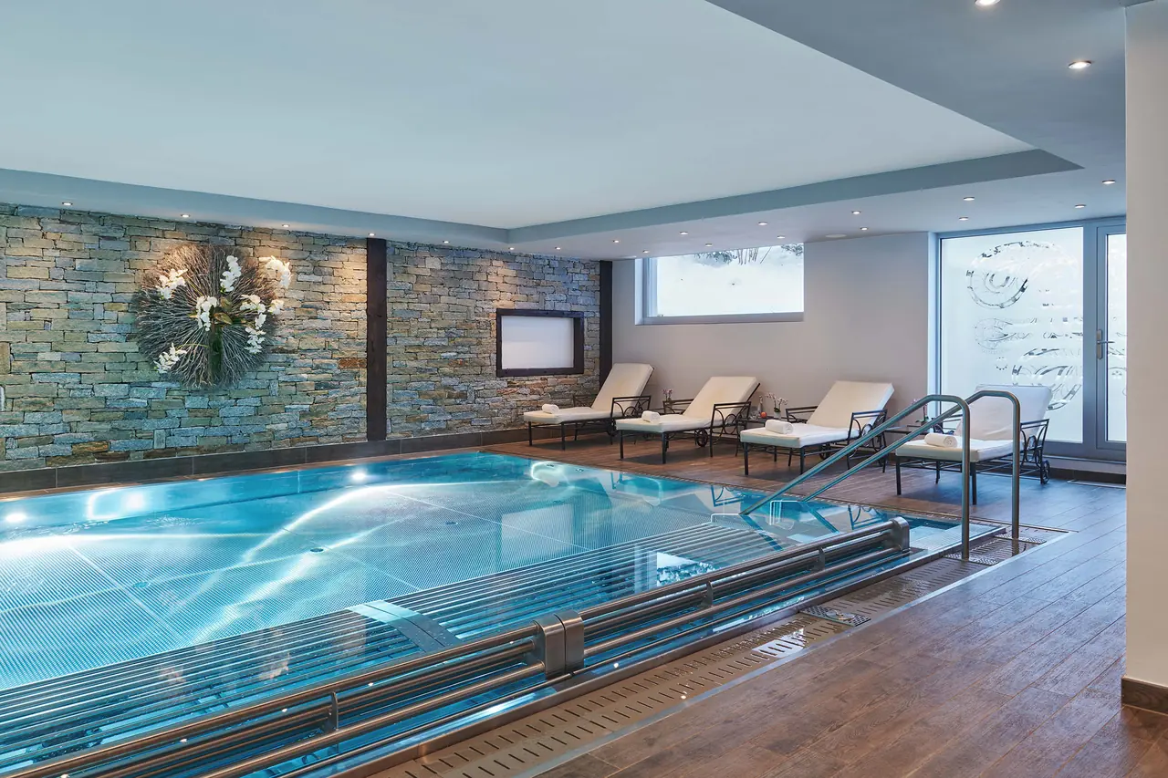 Indoor-Pool mit Liegestühlen am Beckenrand im SCHLOSS Spa Zermatt